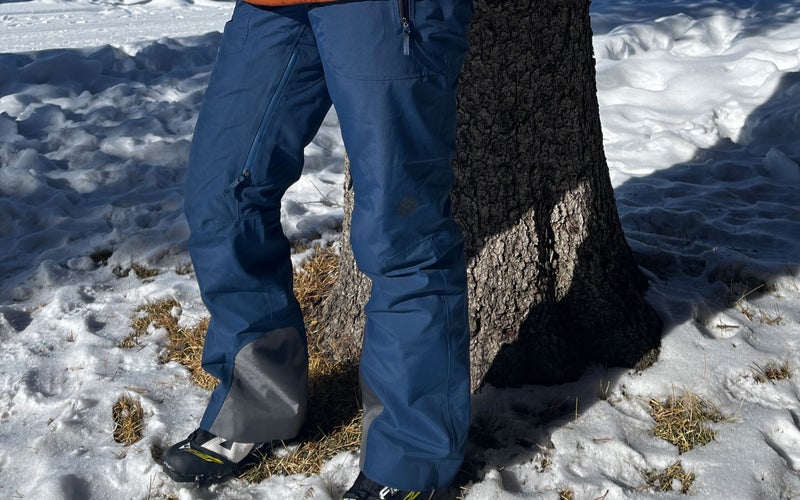 A person wearing Stio women's snow pants in front of a tree with snow on the ground