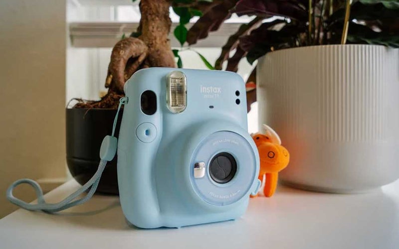Blue Instax Mini sitting on a countertop in front of a plant
